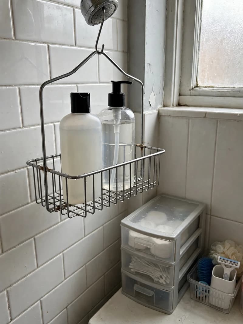 Wire shower caddy hanging from a shower head holding shampoo and body wash bottles against a tiled wall