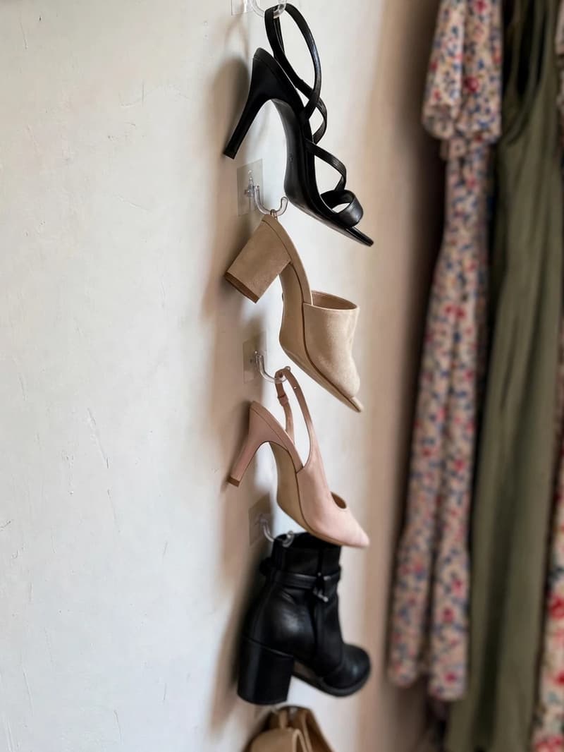 A vertical row of adhesive hooks on a closet side wall holding heeled shoes and flats beside hanging dresses and a mirror